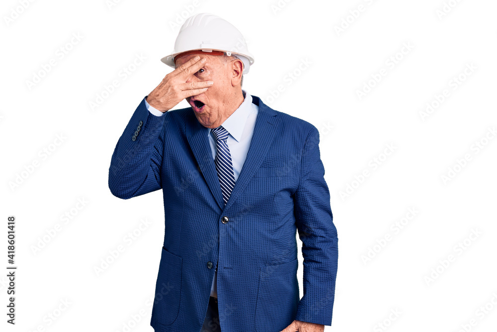 Senior handsome grey-haired man wearing suit and architect hardhat peeking in shock covering face and eyes with hand, looking through fingers with embarrassed expression. Senior handsome grey-haired man wearing suit and architect hardhat peeking in shock covering face and eyes with hand, looking through fingers with embarrassed expression.