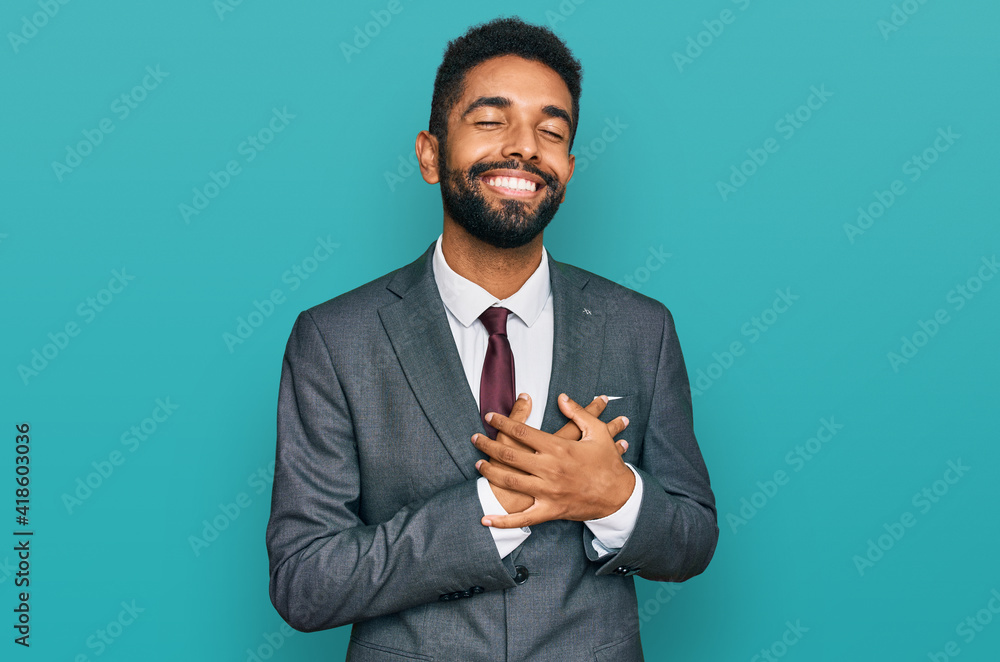 Young african american man wearing business clothes smiling with hands on chest with closed eyes and grateful gesture on face. health concept. Young african american man wearing business clothes smiling with hands on chest with closed eyes and grateful gesture on face. health concept.