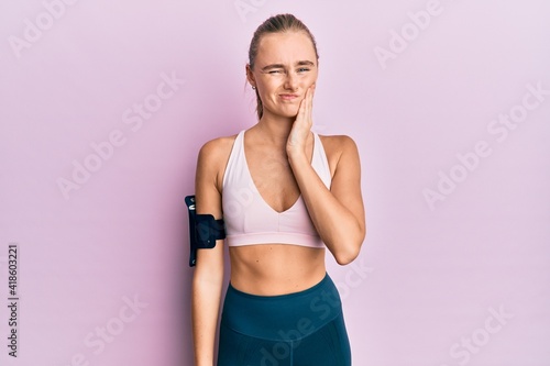 Beautiful blonde woman wearing sportswear and arm band touching mouth with hand with painful expression because of toothache or dental illness on teeth. dentist