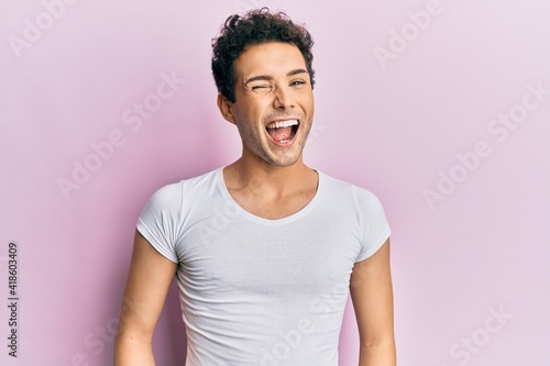Young handsome man wearing casual white t shirt winking looking at the camera with sexy expression, cheerful and happy face.