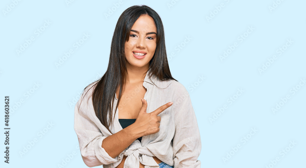 Young beautiful hispanic girl wearing casual clothes cheerful with a smile on face pointing with hand and finger up to the side with happy and natural expression Young beautiful hispanic girl wearing casual clothes cheerful with a smile on face pointing with hand and finger up to the side with happy and natural expression