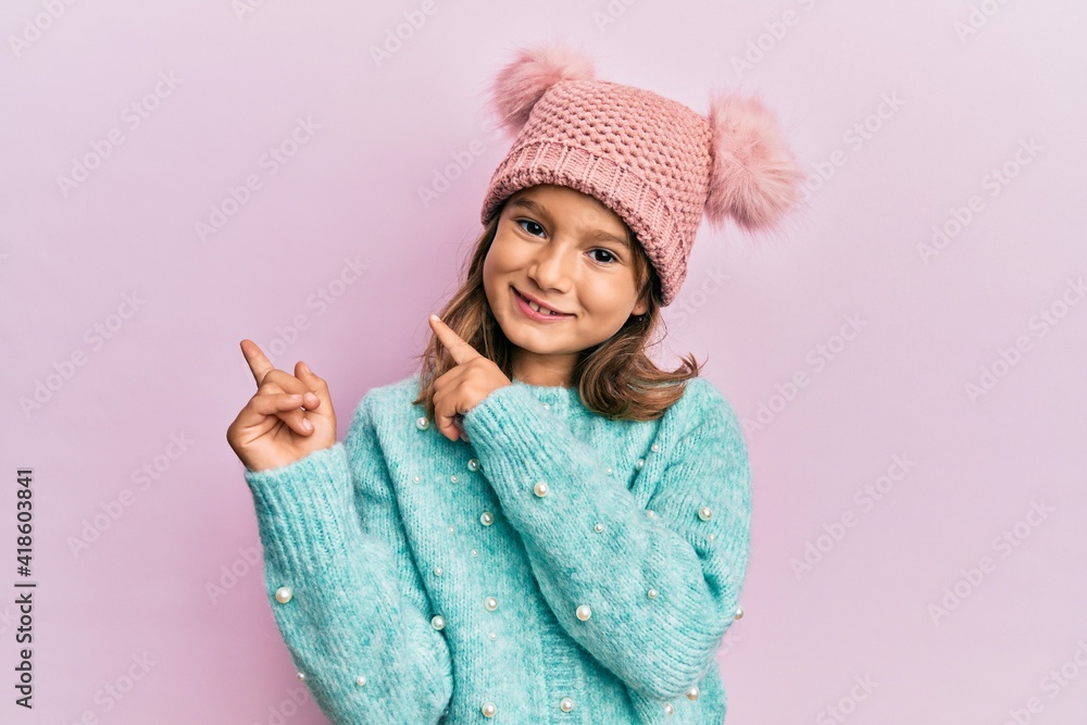 Little beautiful girl wearing wool sweater and cute winter hat smiling and looking at the camera pointing with two hands and fingers to the side. Little beautiful girl wearing wool sweater and cute winter hat smiling and looking at the camera pointing with two hands and fingers to the side.