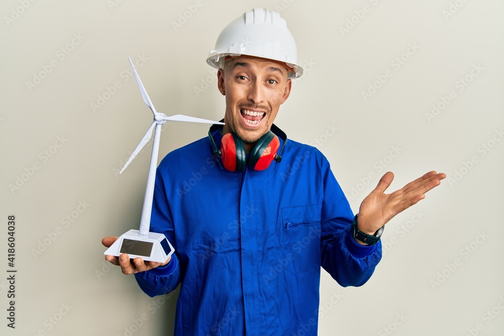 Bald engineer man with beard holding solar windmill for renewable electricity celebrating achievement with happy smile and winner expression with raised hand Bald engineer man with beard holding solar windmill for renewable electricity celebrating achievement with happy smile and winner expression with raised hand