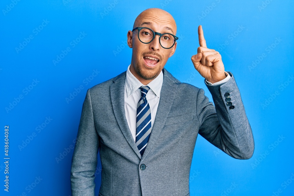 Bald man with beard wearing business jacket and glasses pointing finger up with successful idea. exited and happy. number one. Bald man with beard wearing business jacket and glasses pointing finger up with successful idea. exited and happy. number one.