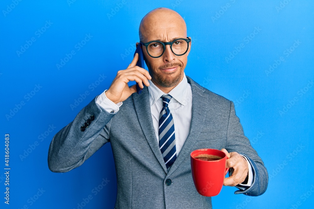Bald man with beard using smartphone and drinking a cup of coffee skeptic and nervous, frowning upset because of problem. negative person. Bald man with beard using smartphone and drinking a cup of coffee skeptic and nervous, frowning upset because of problem. negative person.