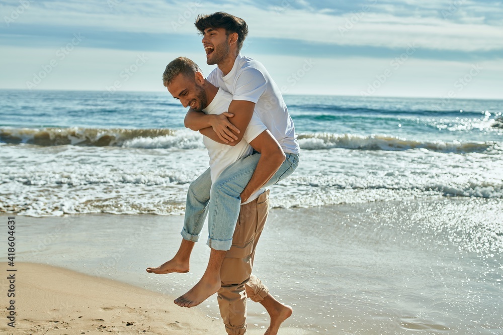 Lovely gay couple on piggyback ride at the beach. Stock Photo