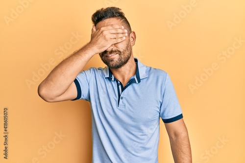 Handsome man with beard wearing casual clothes smiling and laughing with hand on face covering eyes for surprise. blind concept.