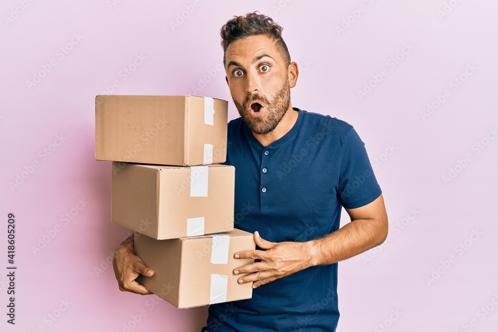 Handsome man with beard holding delivery packages scared and amazed with open mouth for surprise, disbelief face Handsome man with beard holding delivery packages scared and amazed with open mouth for surprise, disbelief face