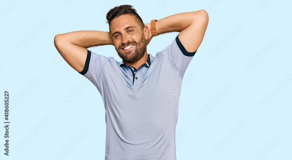Handsome man with beard wearing casual clothes relaxing and stretching, arms and hands behind head and neck smiling happy Handsome man with beard wearing casual clothes relaxing and stretching, arms and hands behind head and neck smiling happy