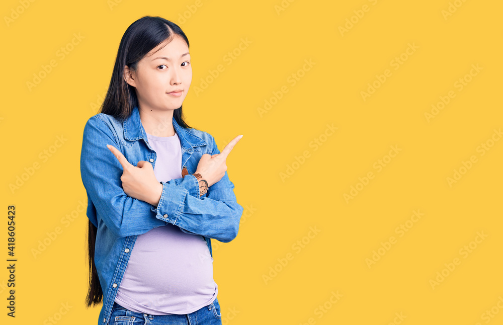 Young beautiful chinese woman pregnant expecting baby pointing to both sides with fingers, different direction disagree Young beautiful chinese woman pregnant expecting baby pointing to both sides with fingers, different direction disagree