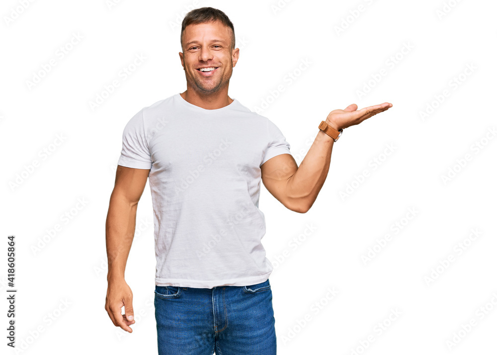 Handsome muscle man wearing casual white tshirt smiling cheerful presenting and pointing with palm of hand looking at the camera. Handsome muscle man wearing casual white tshirt smiling cheerful presenting and pointing with palm of hand looking at the camera.