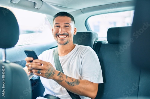 Young hispanic man smiling happy using smartphone sitting on the car.