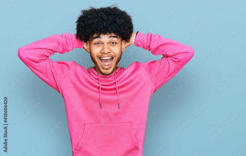 Young african american man with afro hair wearing casual pink sweatshirt crazy and scared with hands on head, afraid and surprised of shock with open mouth Young african american man with afro hair wearing casual pink sweatshirt crazy and scared with hands on head, afraid and surprised of shock with open mouth