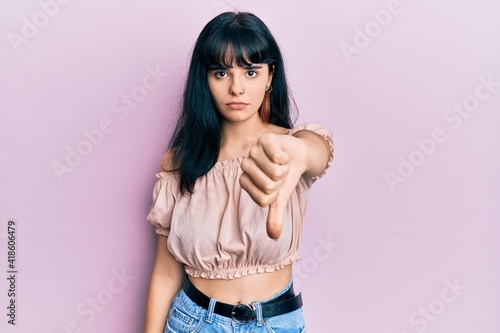 Young hispanic girl wearing casual clothes looking unhappy and angry showing rejection and negative with thumbs down gesture. bad expression.