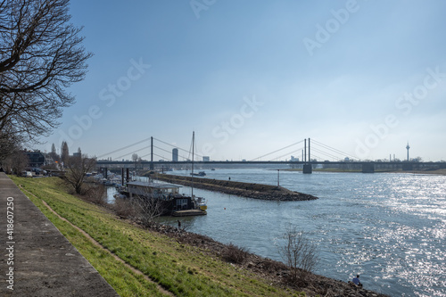 Outdoor sunny view along promenade riverside, pier and harbour on Rhine River and background cityscape, suspension bridge and Rhine tower in Düsseldorf, Germany.