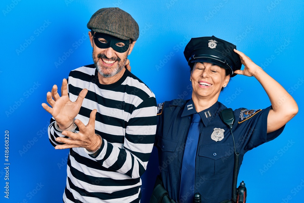 Middle age couple of hispanic woman and man wearing thief and police uniform smiling confident touching hair with hand up gesture, posing attractive and fashionable Middle age couple of hispanic woman and man wearing thief and police uniform smiling confident touching hair with hand up gesture, posing attractive and fashionable