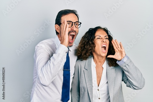 Middle age couple of hispanic woman and man wearing business office uniform shouting and screaming loud to side with hand on mouth. communication concept.