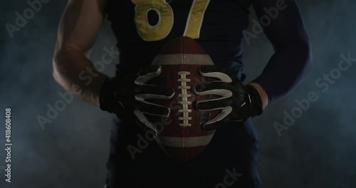 American football sportsman player holding a ball on black background close up