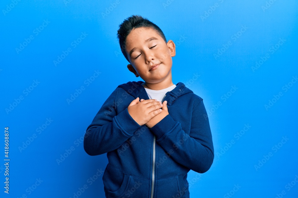 Little boy hispanic kid wearing casual sporty jacket smiling with hands on chest, eyes closed with grateful gesture on face. health concept. Little boy hispanic kid wearing casual sporty jacket smiling with hands on chest, eyes closed with grateful gesture on face. health concept.
