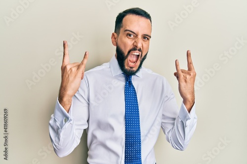 Young man with beard wearing business tie shouting with crazy expression doing rock symbol with hands up. music star. heavy concept.