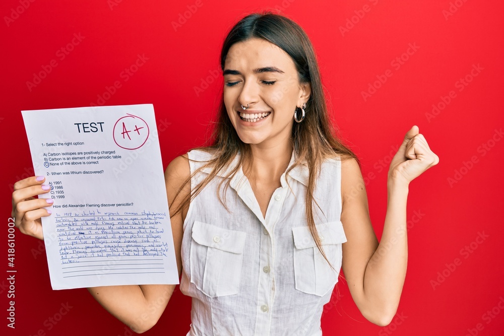 Young hispanic woman showing a passed exam holding trophy screaming proud, celebrating victory and success very excited with raised arm Young hispanic woman showing a passed exam holding trophy screaming proud, celebrating victory and success very excited with raised arm