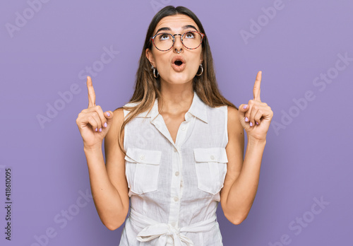 Young hispanic woman wearing casual clothes amazed and surprised looking up and pointing with fingers and raised arms.