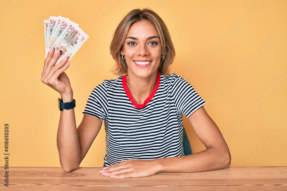 Beautiful caucasian woman holding yuan chinese banknotes looking positive and happy standing and smiling with a confident smile showing teeth Beautiful caucasian woman holding yuan chinese banknotes looking positive and happy standing and smiling with a confident smile showing teeth