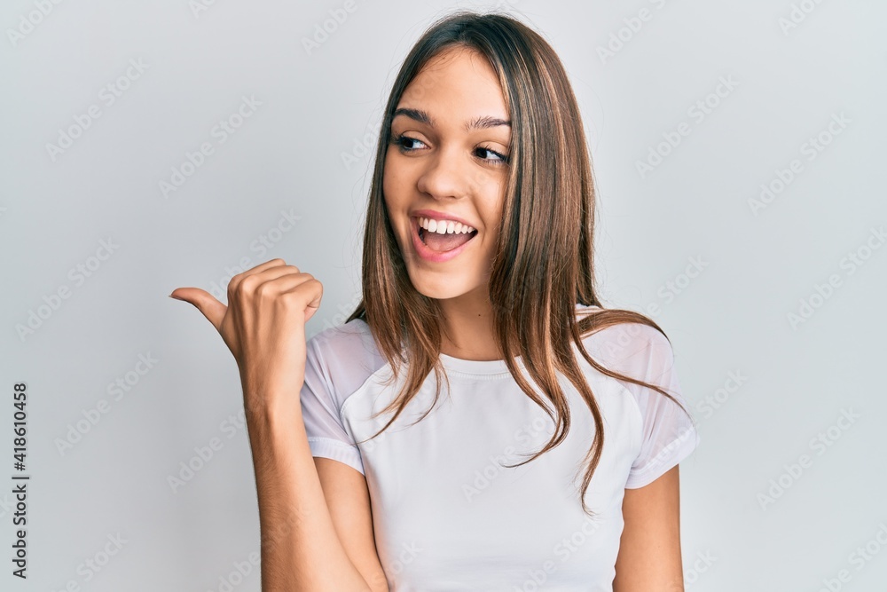 Young brunette woman wearing casual white t shirt pointing thumb up to the side smiling happy with open mouth Young brunette woman wearing casual white t shirt pointing thumb up to the side smiling happy with open mouth