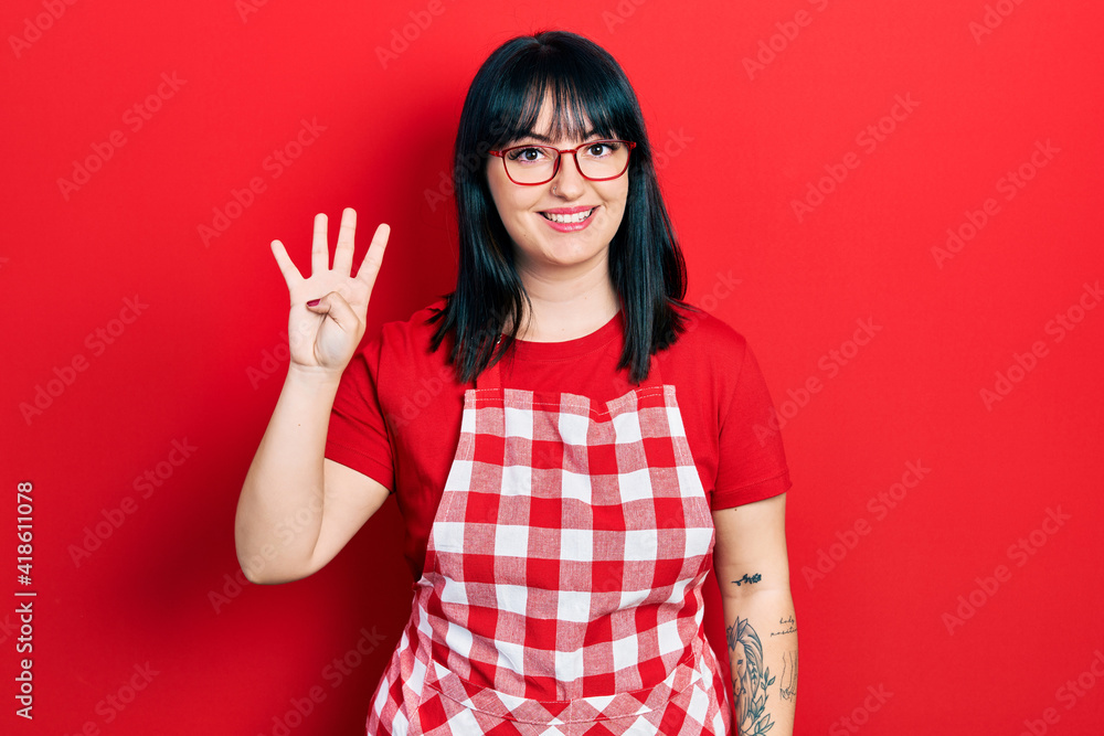 Young hispanic woman wearing cook apron and glasses showing and pointing up with fingers number four while smiling confident and happy. Young hispanic woman wearing cook apron and glasses showing and pointing up with fingers number four while smiling confident and happy.