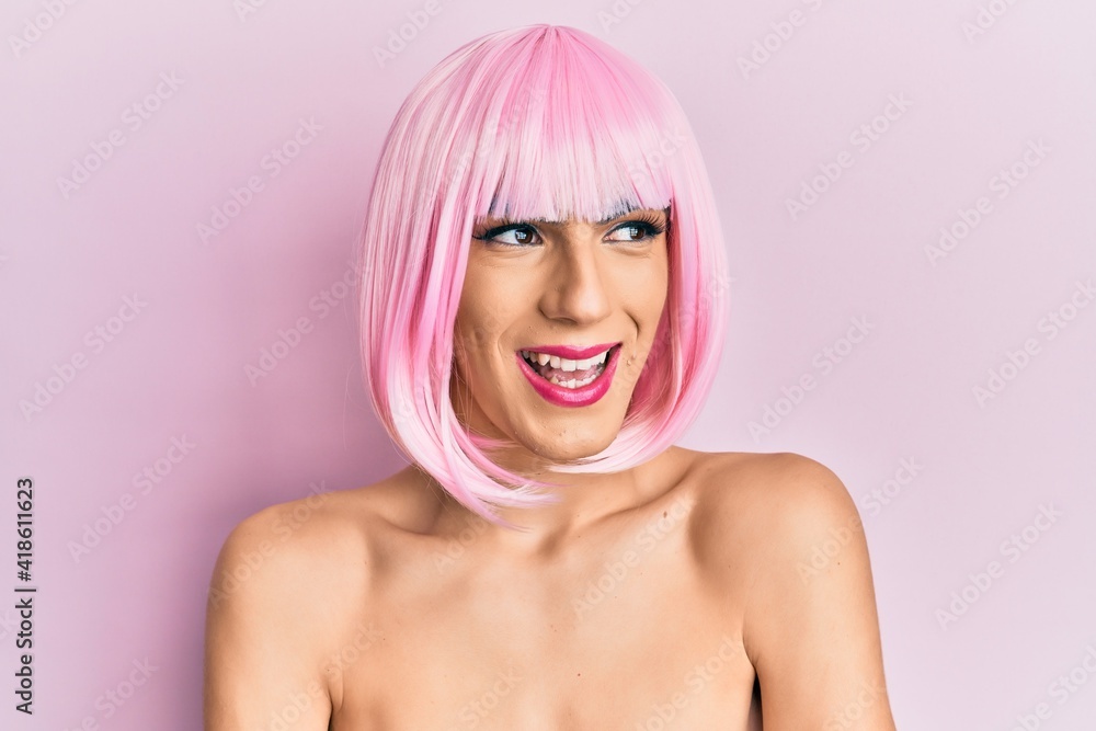 Young man wearing woman make up wearing pink wig smiling looking to the side and staring away thinking. Young man wearing woman make up wearing pink wig smiling looking to the side and staring away thinking.