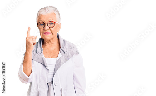 Senior beautiful woman with blue eyes and grey hair wearing casual clothes and glasses showing and pointing up with finger number one while smiling confident and happy.