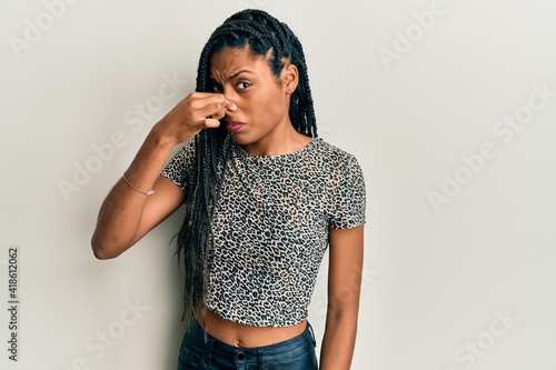 African american woman wearing casual clothes smelling something stinky and disgusting, intolerable smell, holding breath with fingers on nose. bad smell