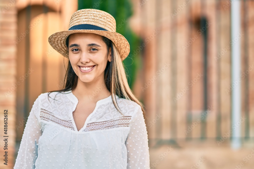 Young hispanic tourist woman wearing summer hat standing at the city.