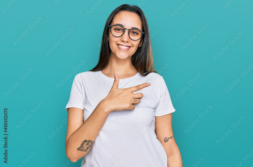 Young hispanic woman wearing casual white t shirt cheerful with a smile on face pointing with hand and finger up to the side with happy and natural expression Young hispanic woman wearing casual white t shirt cheerful with a smile on face pointing with hand and finger up to the side with happy and natural expression
