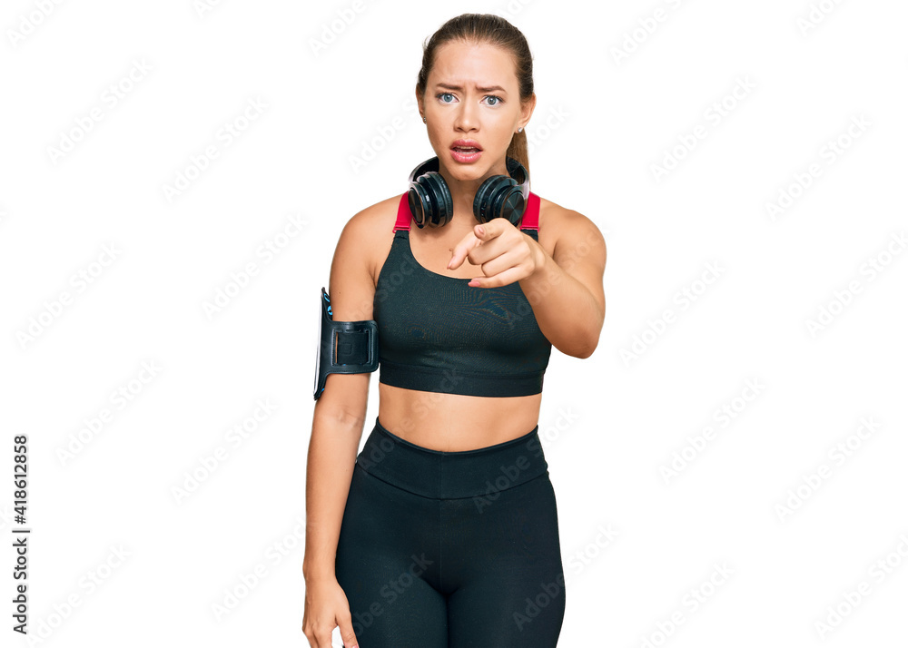 Beautiful blonde woman wearing gym clothes and using headphones pointing displeased and frustrated to the camera, angry and furious with you Beautiful blonde woman wearing gym clothes and using headphones pointing displeased and frustrated to the camera, angry and furious with you