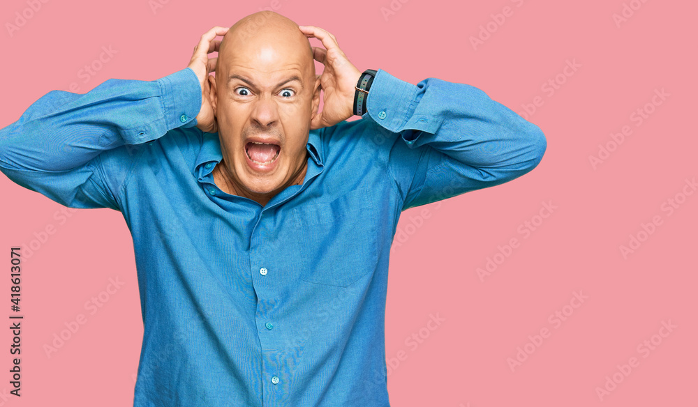 Middle age bald man wearing casual clothes crazy and scared with hands on head, afraid and surprised of shock with open mouth Middle age bald man wearing casual clothes crazy and scared with hands on head, afraid and surprised of shock with open mouth