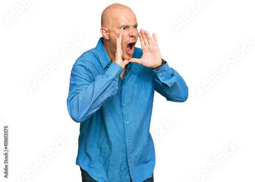 Middle age bald man wearing casual clothes shouting angry out loud with hands over mouth