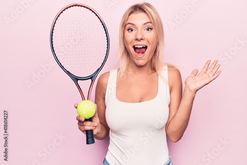 Obraz na płótnie Young beautiful blonde sportswoman playing tennis using racket and ball over pink background celebrating achievement with happy smile and winner expression with raised hand w salonie