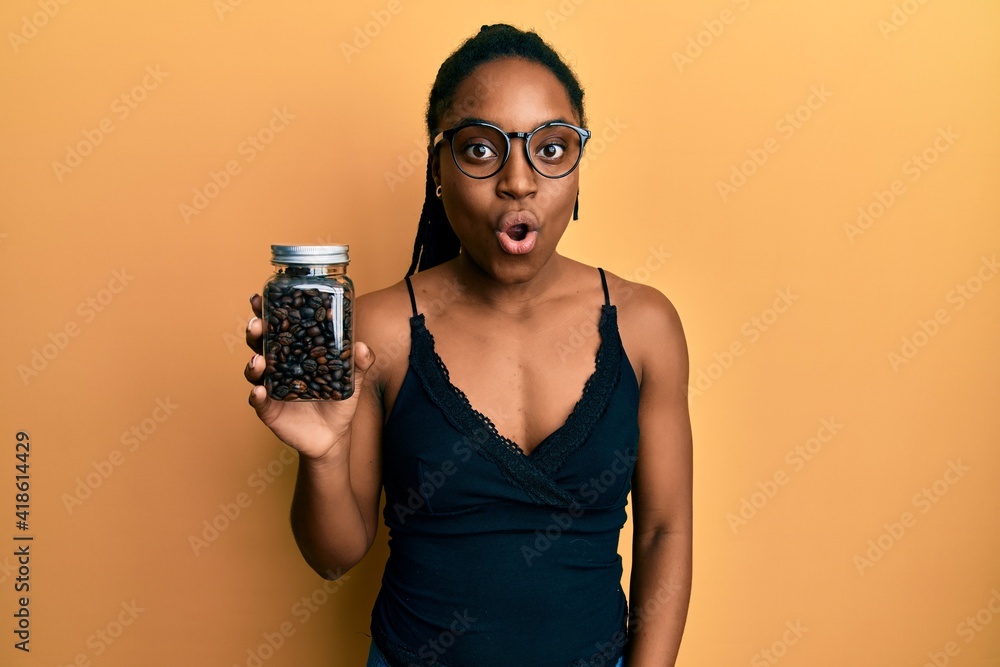 African american woman with braided hair holding jar with coffee beans scared and amazed with open mouth for surprise, disbelief face African american woman with braided hair holding jar with coffee beans scared and amazed with open mouth for surprise, disbelief face