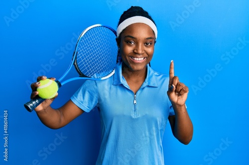 African american woman with braided hair playing tennis holding racket and ball smiling with an idea or question pointing finger with happy face, number one © Krakenimages.com