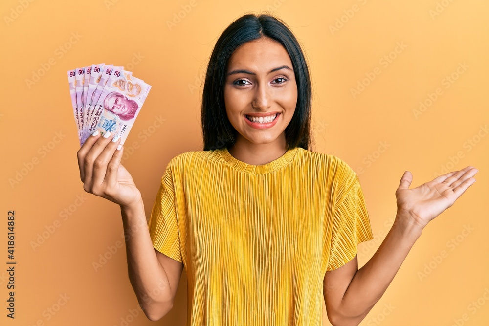 Young brunette woman holding 50 mexican pesos banknotes celebrating achievement with happy smile and winner expression with raised hand Young brunette woman holding 50 mexican pesos banknotes celebrating achievement with happy smile and winner expression with raised hand