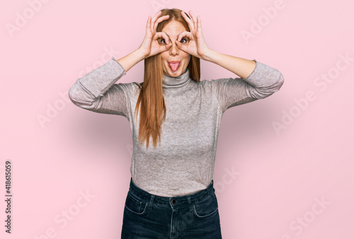 Young irish woman wearing casual clothes doing ok gesture like binoculars sticking tongue out, eyes looking through fingers. crazy expression.