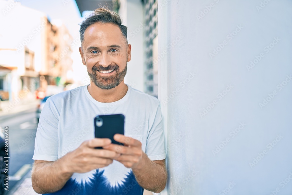 Middle age handsome man smiling happy using smartphone at the city.