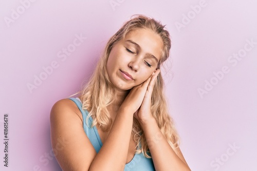 Young blonde girl wearing casual clothes sleeping tired dreaming and posing with hands together while smiling with closed eyes.