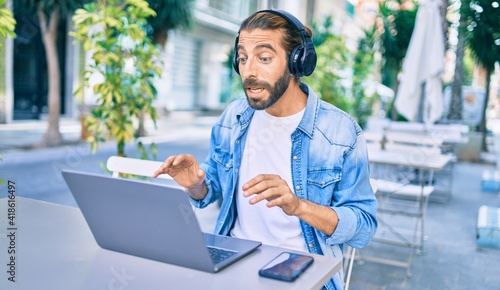 Young middle eastern man doing video call using laptop and headphones at coffee shop terrace. © Krakenimages.com