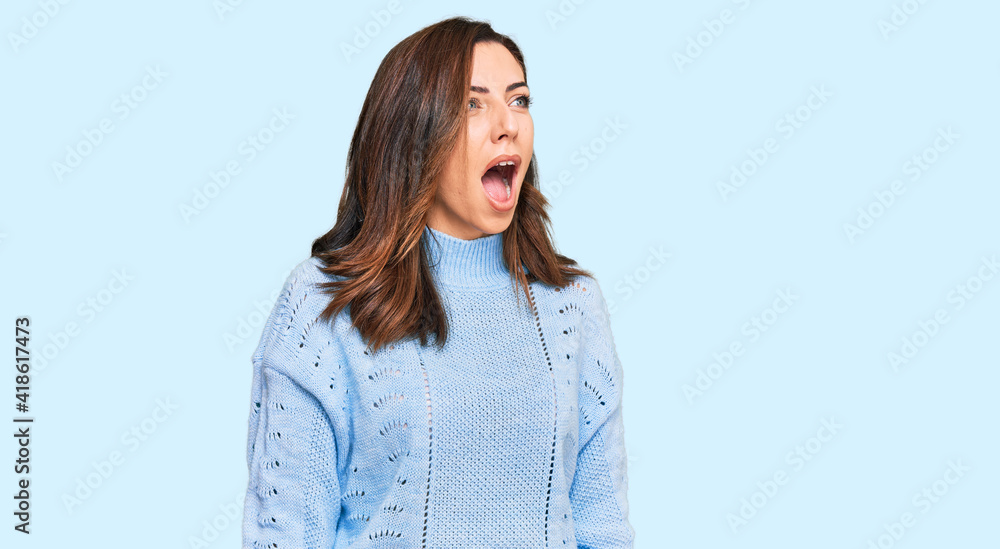 Fototapeta premium Young brunette woman wearing casual winter sweater angry and mad screaming frustrated and furious, shouting with anger. rage and aggressive concept.