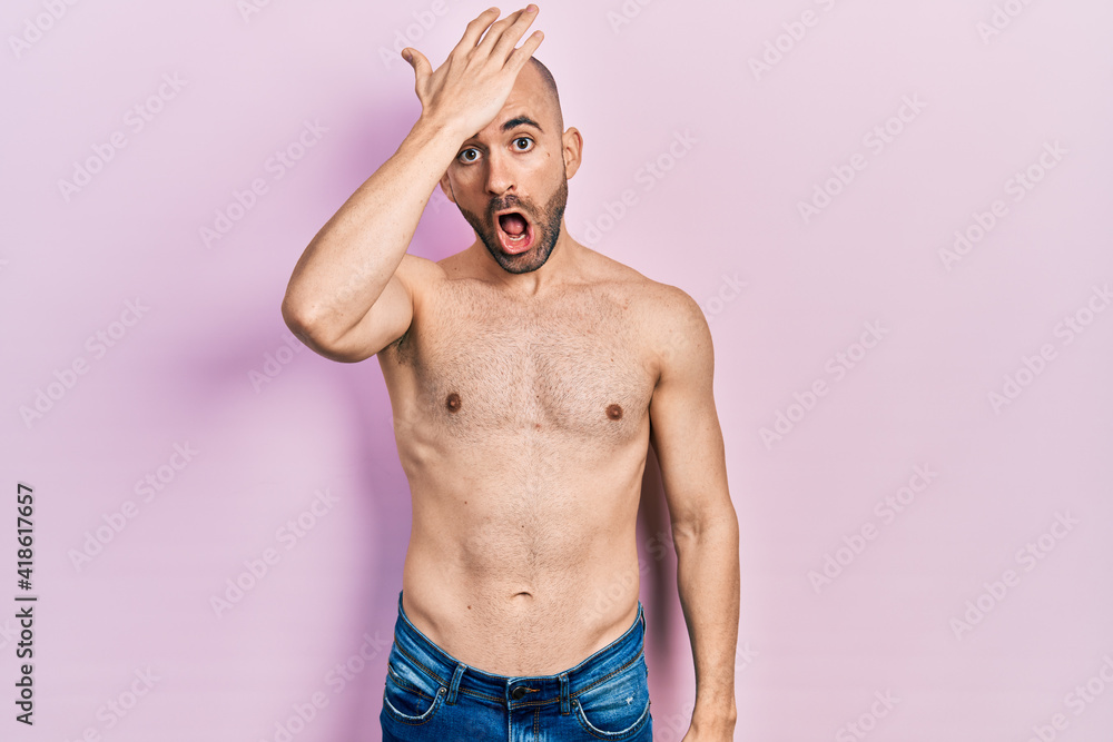 Fototapeta premium Young bald man standing shirtless surprised with hand on head for mistake, remember error. forgot, bad memory concept.