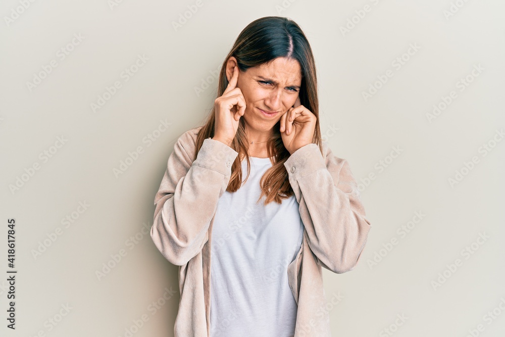 Brunette young woman wearing casual clothes covering ears with fingers with annoyed expression for the noise of loud music. deaf concept. Brunette young woman wearing casual clothes covering ears with fingers with annoyed expression for the noise of loud music. deaf concept.