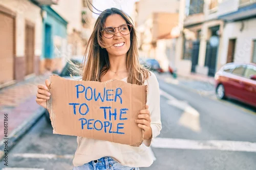 Obraz Young caucasian woman smiling happy holding power to the people banner cardboard walking at the city.