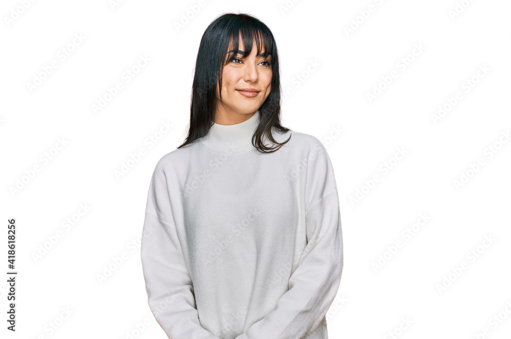 Young brunette woman with bangs wearing casual turtleneck sweater looking away to side with smile on face, natural expression. laughing confident. Young brunette woman with bangs wearing casual turtleneck sweater looking away to side with smile on face, natural expression. laughing confident.